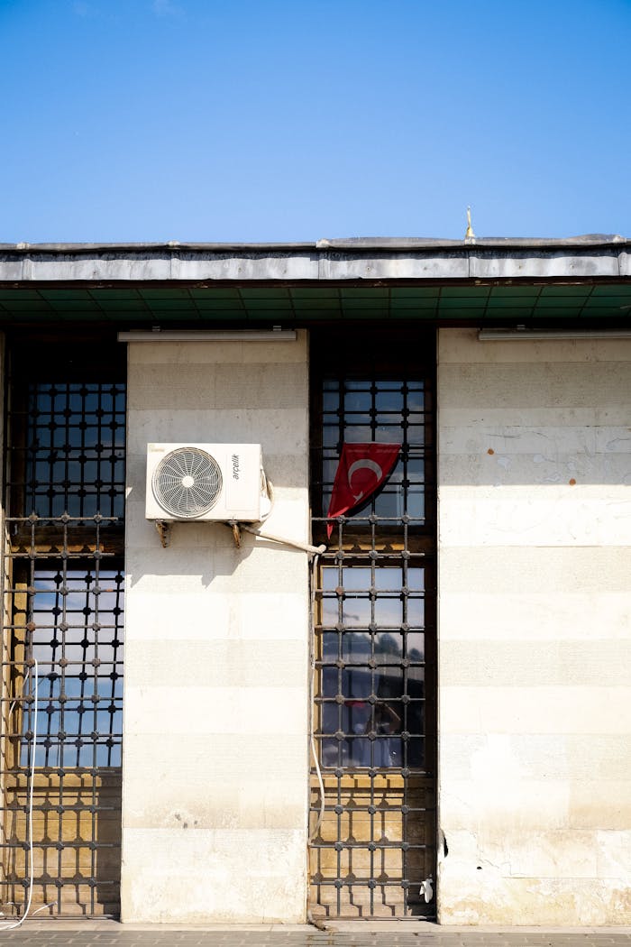 Facade of a building with air conditioning unit and Turkish flag under a clear blue sky.